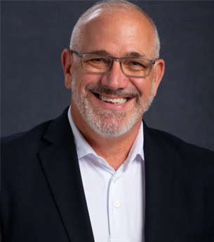 Experienced business professional smiling, wearing glasses and a suit, representing United Franchise Group's leadership in franchising and business solutions.